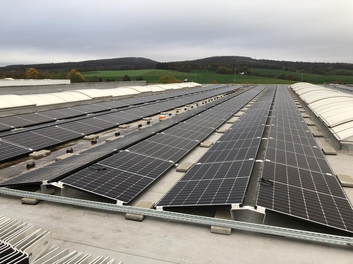 Solaranlagen auf einem Dach mit bedecktem Himmel und Hügeln im Hintergrund.