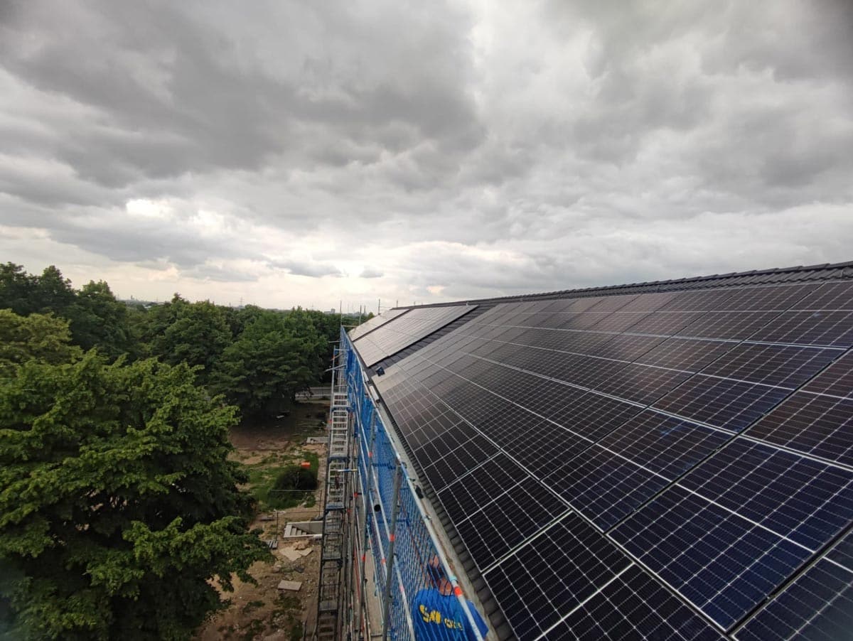 Solarpanele auf einem Dach unter bewölktem Himmel, umgeben von grünen Bäumen.